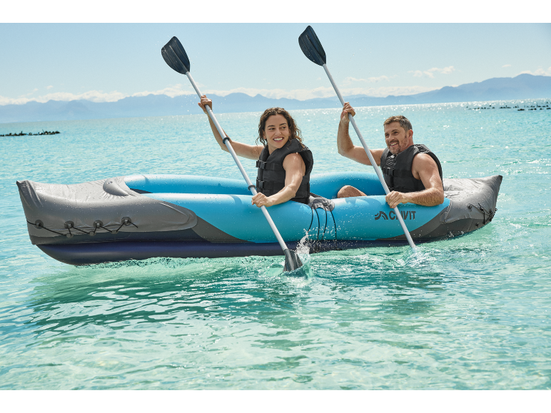 Deux personnes souriantes en gilets de sauvetage pagayant dans un kayak gonflable bleu sur l'eau.