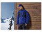 Homme en veste de ski bleue avec des skis en arrière-plan.