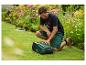 Homme agenouillé sur l'herbe, souriant et interagissant avec une tondeuse robot dans un jardin.