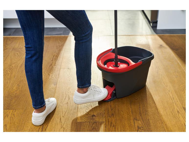 Personne en jean et chaussures blanches utilisant une serpillière avec seau à pédale.