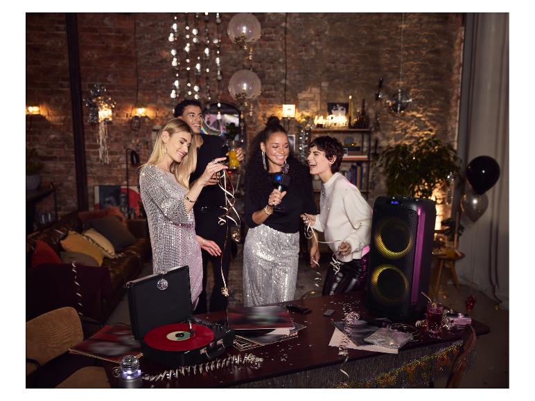 Groupe d'amis en fête avec platine vinyle, enceinte et décorations festives.