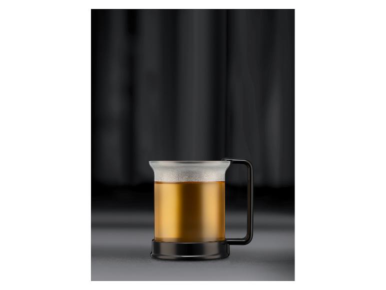 Mug en verre avec une anse noire, rempli de liquide ambré, sur fond sombre.