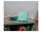 Une lampe de chevet en forme de poulpe verte sur une table de chevet avec des jouets et des livres.