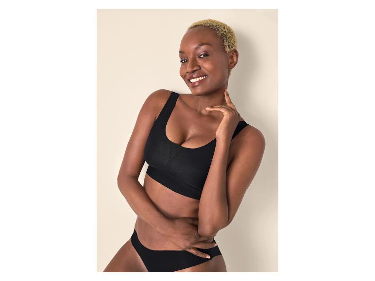 Femme souriante aux cheveux blonds courts, main sur le menton, portant un soutien-gorge et une culotte noirs.