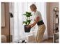 Une femme porte une ceinture de soutien lombaire en soulevant une plante.