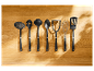 Sept ustensiles de cuisine noirs Zwilling J.A. Henckels disposés sur une surface en bois.