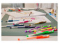 Divers crayons de couleur et stylos de la marque United Office sur une table verte.