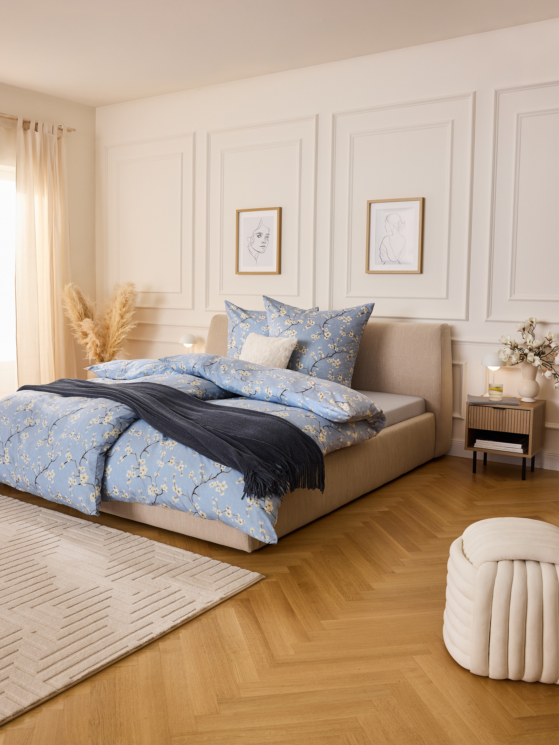 Chambre avec parure de lit bleue à motifs floraux, lit clair et parquet.