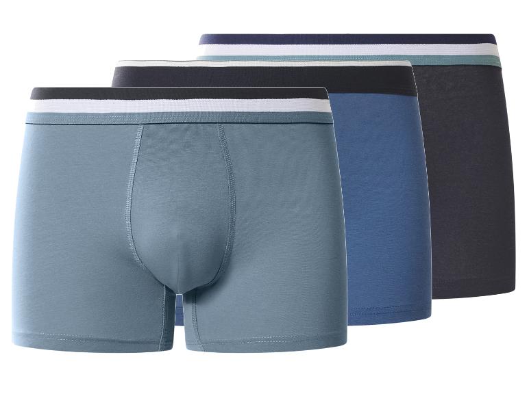 Trois boxers pour hommes dans des tons de bleu et de gris avec des ceintures rayées.