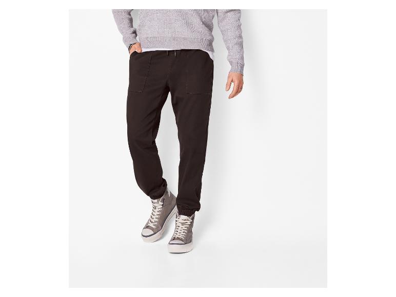 Homme en pull gris, pantalon de jogging noir et baskets montantes grises.