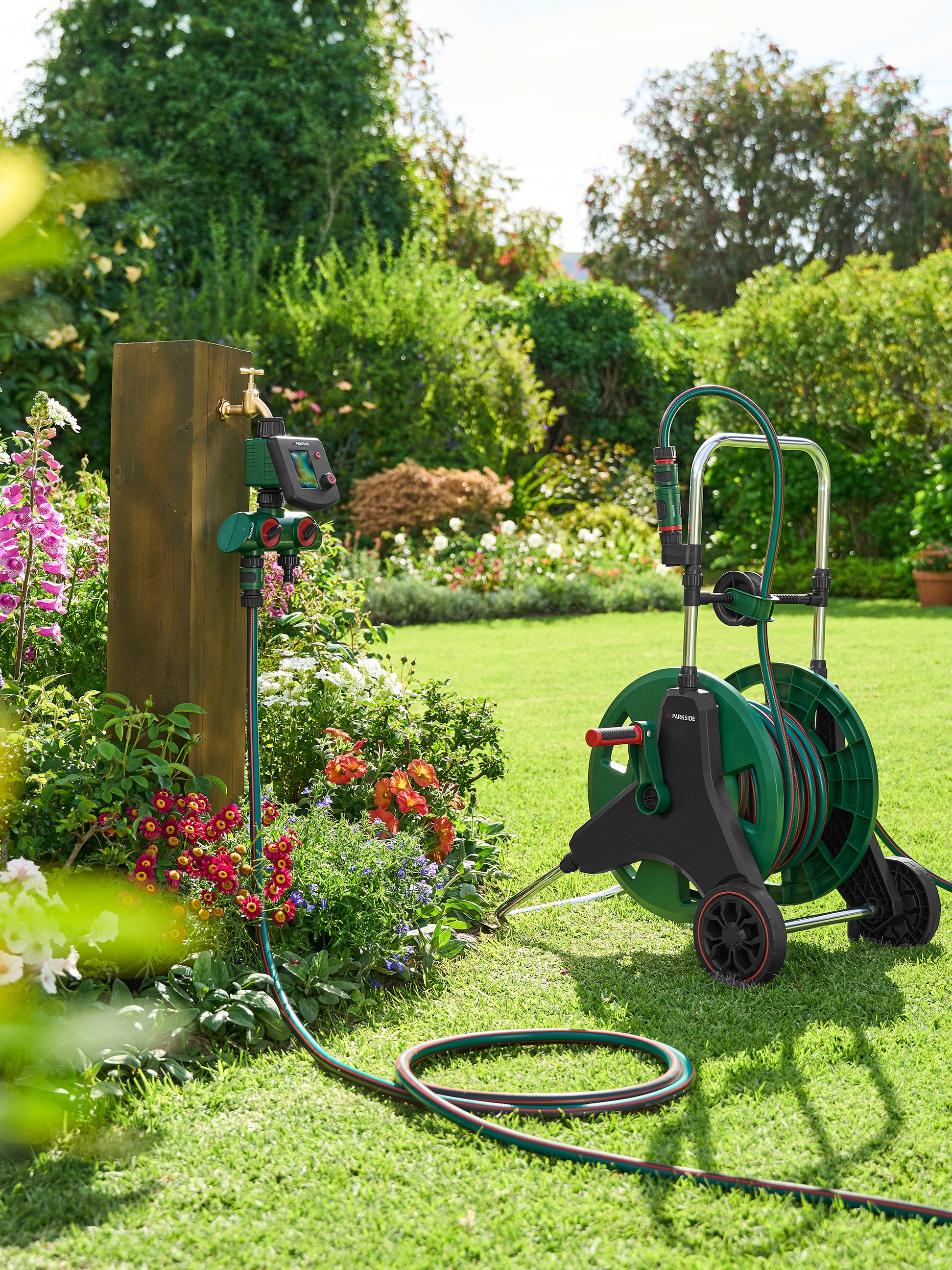 Tuyau d'arrosage sur enrouleur et programmateur d'eau Parkside dans un jardin.