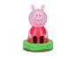 Figurine de cochon en robe rouge sur une base verte avec herbe et fleurs.