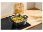 Casserole carrée avec pâtes et légumes sur une plaque à induction, huile et poivre en arrière-plan.