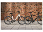 Deux vélos électriques, un blanc et un noir, garés devant un mur de briques.