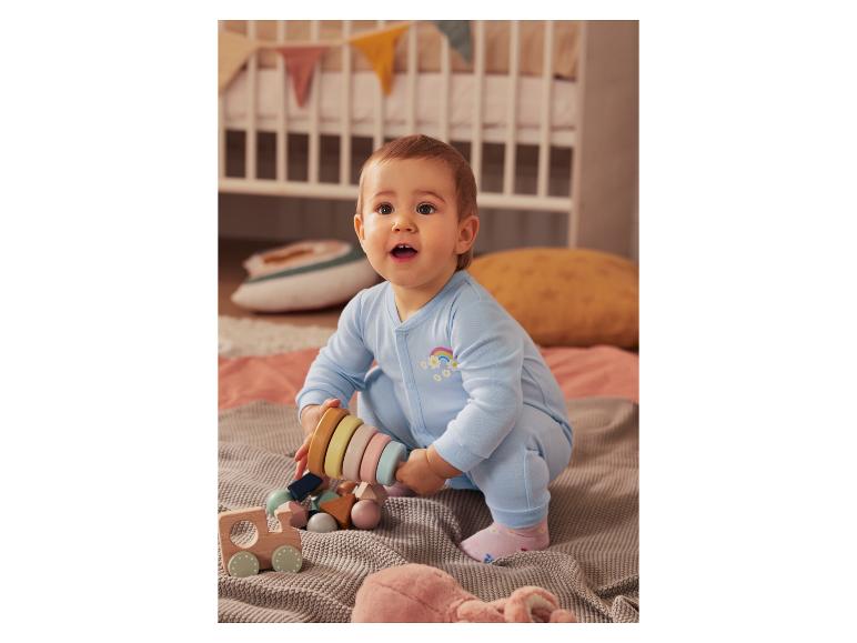 Un bébé en combinaison bleue joue avec des jouets en bois.