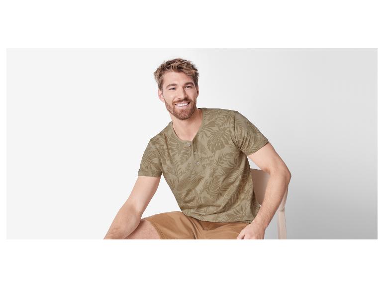 Homme assis sur une chaise avec une chemise beige à motif tropical.