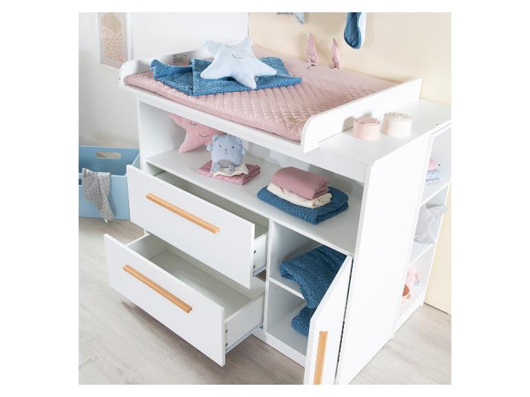 Table à langer blanche avec tiroirs et étagères, décorée d'accessoires et de jouets pour bébé.