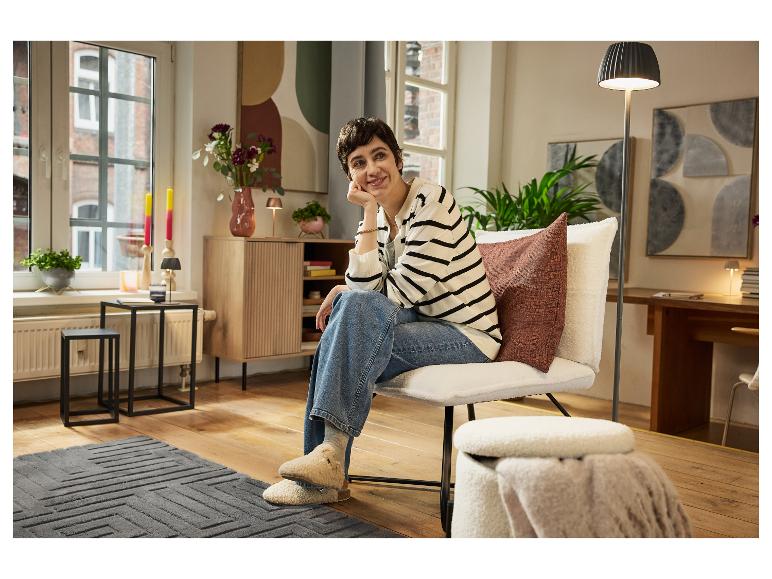 Une femme se détend dans un fauteuil confortable avec un pouf en peau de mouton, entourée d'une décoration intérieure élégante.