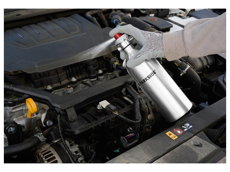 Main gantée pulvérisant du nettoyant sur un moteur de voiture.