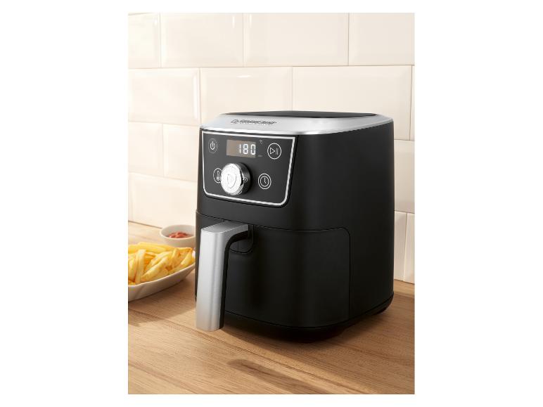 Friteuse à air noire avec écran numérique et frites sur une surface en bois.
