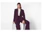 Femme en blazer violet foncé et pantalon assorti, assise sur une boîte blanche.