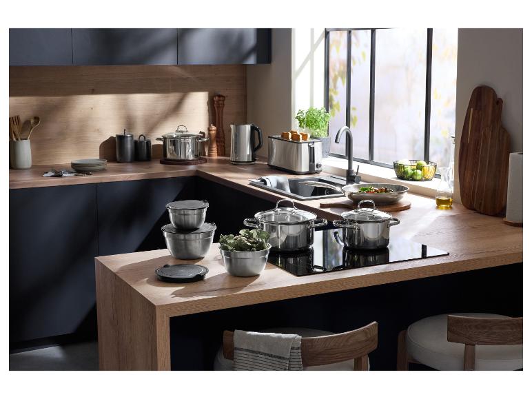 Cuisine moderne avec ustensiles de cuisine en acier inoxydable, grille-pain et bouilloire sur des comptoirs en bois.