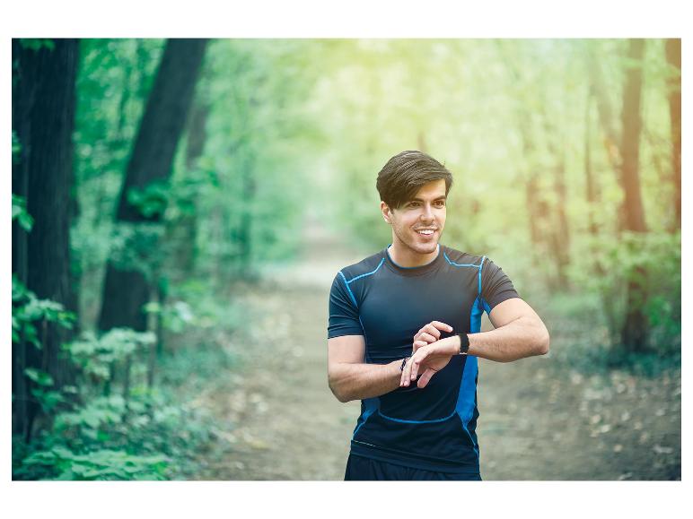 Un homme en vêtements de sport regarde sa montre connectée dans la forêt.
