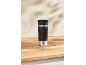 Mug de voyage noir et argent sur une surface en bois avec des grains de café.