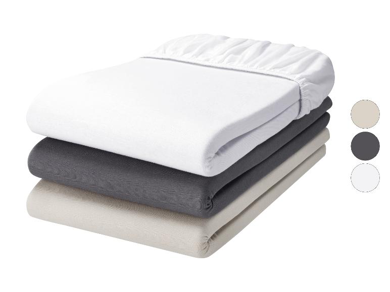 Lot de trois draps-housses en blanc, gris foncé et beige.