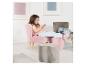 Une fille assise sur une chaise en velours rose, les pieds sur un pouf assorti.