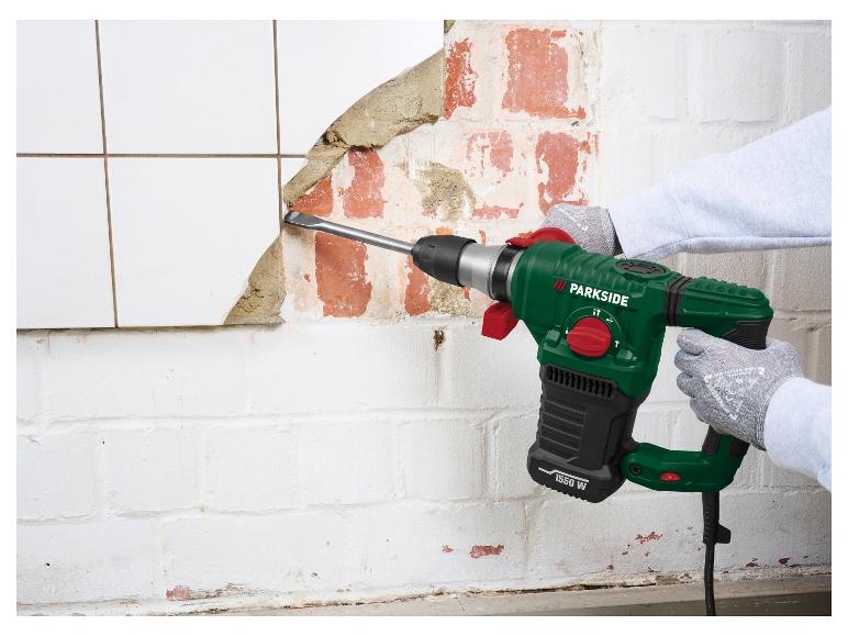 Marteau perforateur électrique vert et noir retirant des carreaux d'un mur de briques.