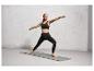 Une femme en brassière de sport et leggings fait du yoga sur un tapis gris.