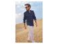 Homme en chemise bleue et pantalon clair marchant sur des dunes de sable.
