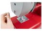 Main enfilant une machine à coudre rouge, le fil passe par le guide-fil.