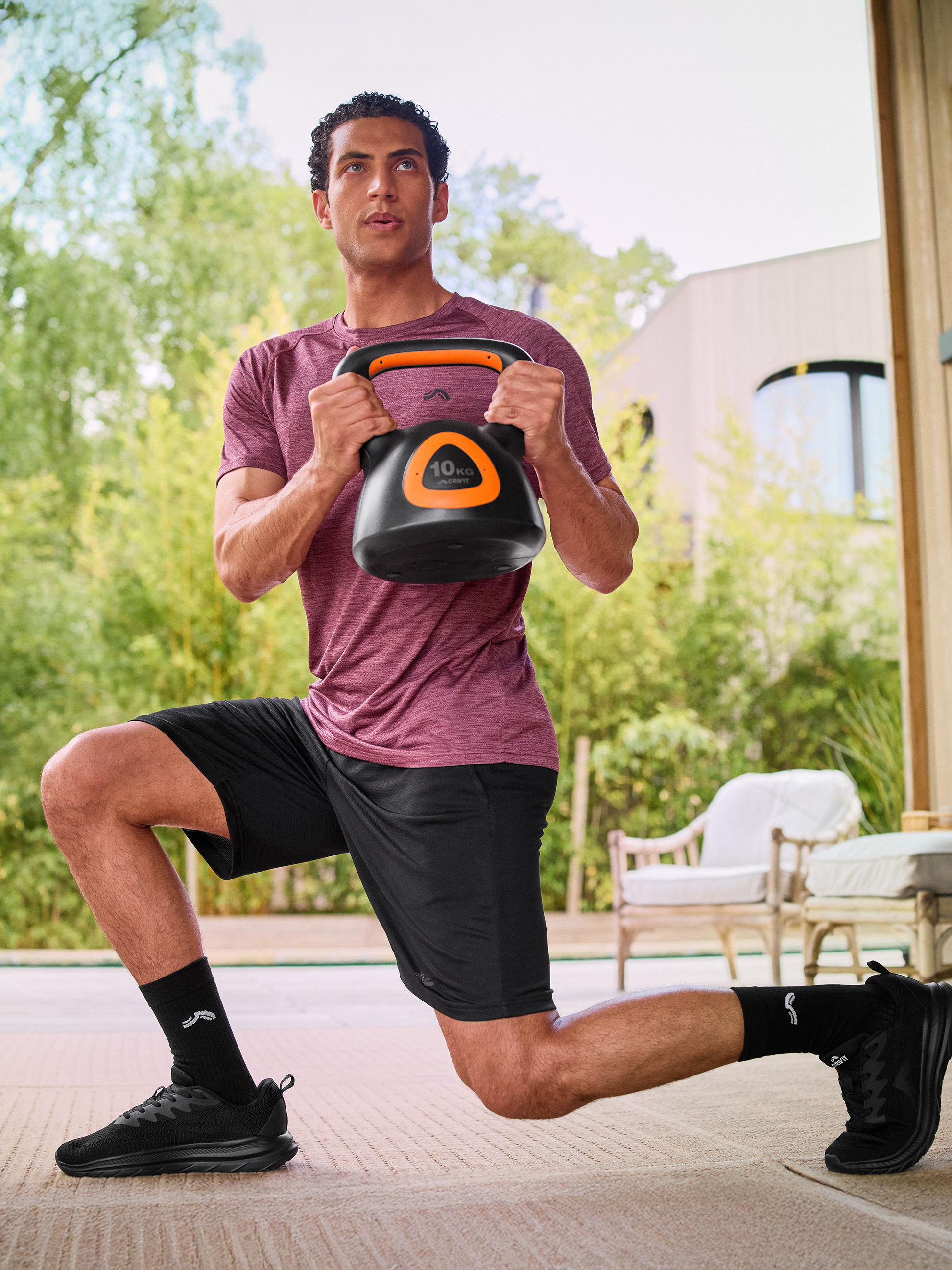 Homme en tenue de sport faisant une fente avec un kettlebell noir de 10 kg.