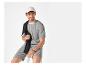 Homme en t-shirt et short rayés, casquette blanche et sweat-shirt noir sur l'épaule.