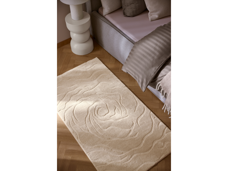 Tapis beige avec motif de roses en relief dans une chambre avec lit et table de chevet.