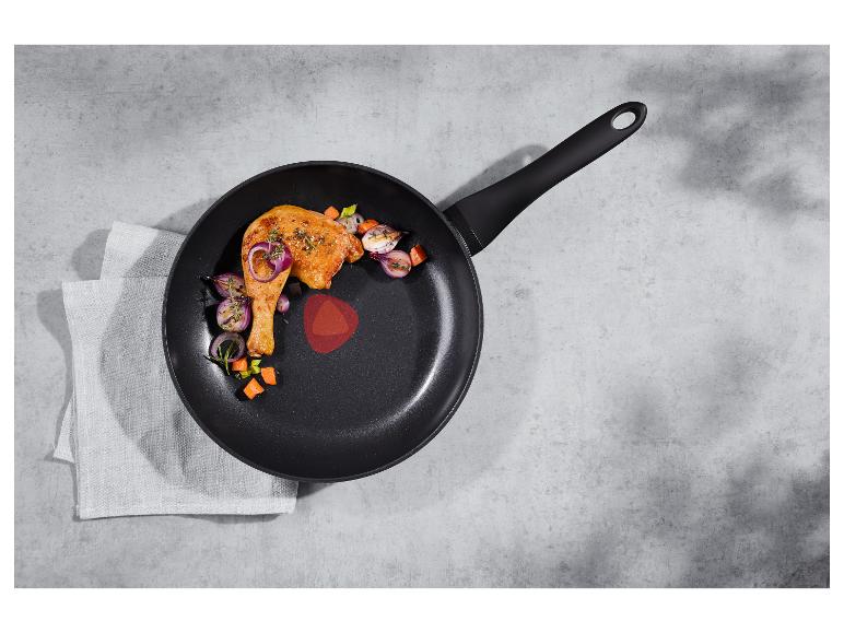 Poêle à frire avec cuisse de poulet et légumes sur fond gris avec un torchon.