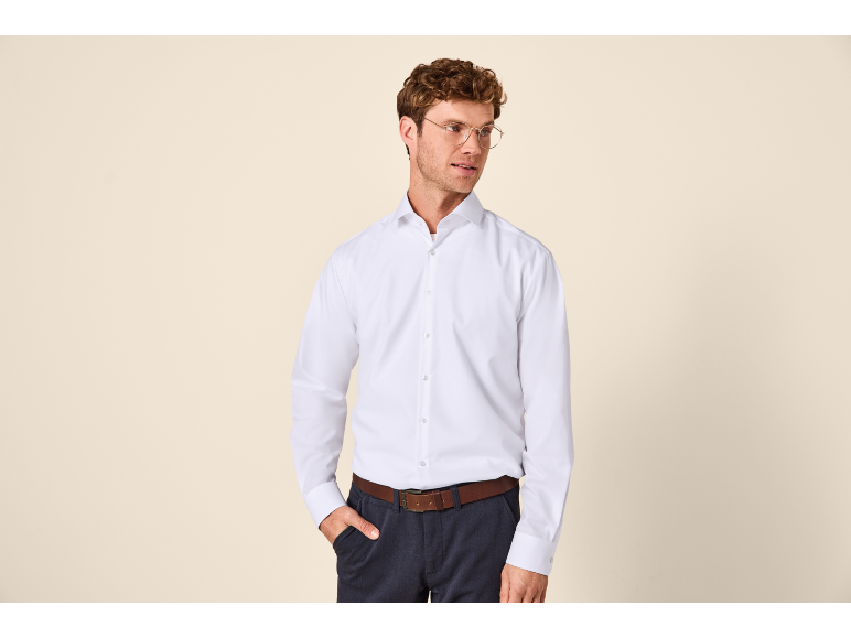 Homme en chemise blanche classique à manches longues et pantalon foncé.