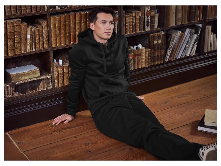 Homme en sweat à capuche et pantalon de survêtement noirs assis sur un plancher en bois dans une bibliothèque.