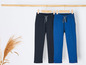 Deux pantalons de survêtement, l'un bleu et l'autre noir, suspendus à un cintre en bois.