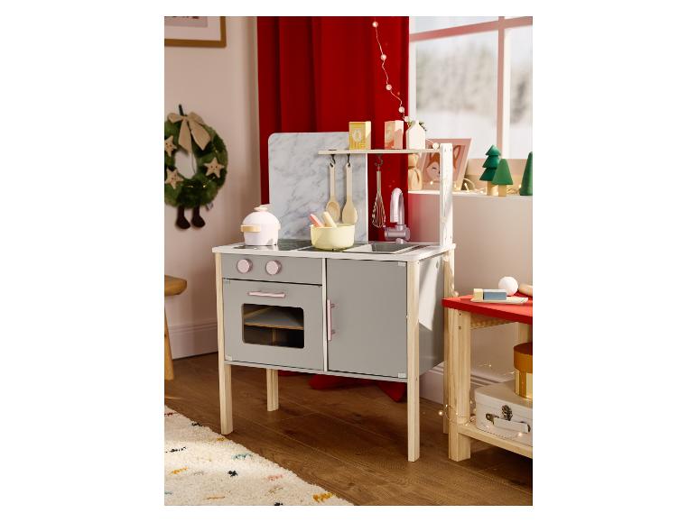 Cuisine de jeu en bois grise et blanche avec accessoires dans une pièce décorée pour les fêtes.
