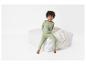 Un enfant portant un pyjama vert avec un motif de dinosaure assis sur un coussin blanc.