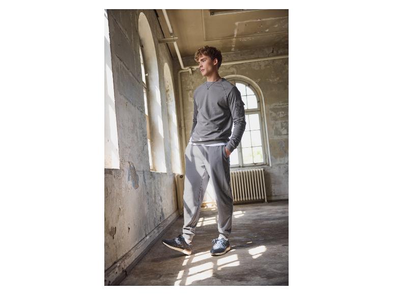 Homme en sweat-shirt gris et pantalon de jogging New Balance dans un bâtiment abandonné.
