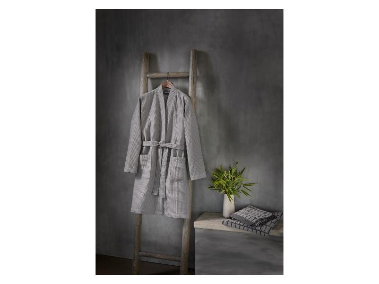 Peignoir gaufré gris sur une échelle en bois, avec des serviettes et une plante sur une table d'appoint.