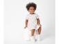 Une petite fille portant une robe blanche à motifs de citrons et des baskets blanches.