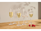 Six flûtes à champagne, certaines remplies de vin mousseux, et trois framboises sur une table en bois.