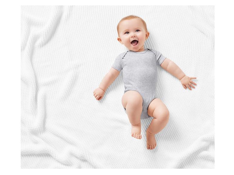 Bébé souriant sur un plaid blanc, vêtu d'un body gris.