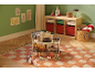 Maison de poupée avec meubles et poupées sur un tapis à carreaux dans une chambre d'enfant.