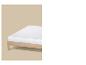 Un matelas blanc sur un cadre de lit en bois clair sur fond beige.